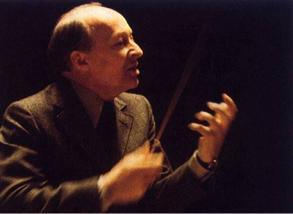 Zdjęcie przedstawia Witolda Lutosławskiego jako dyrygenta. Tło ciemne, w tonacji ciemnobrązowej.