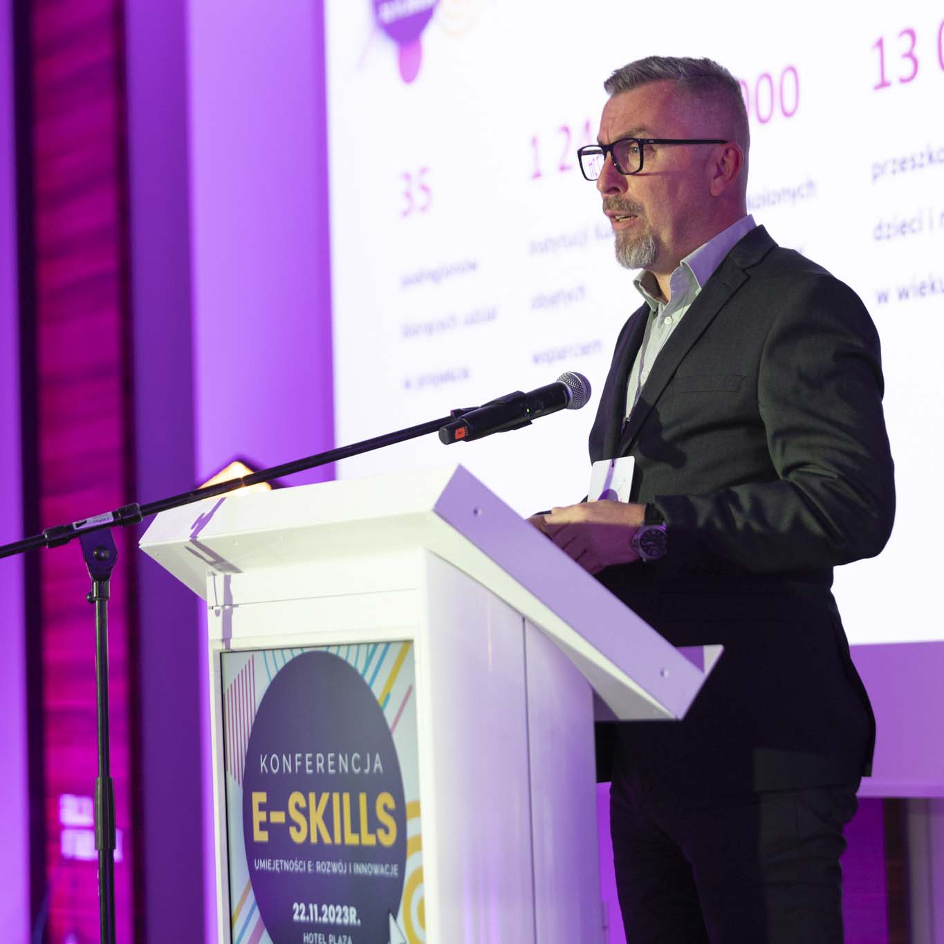 Przy mównicy stoi Pan Norbert Ogłaza. Wzrok kieruje w stronę uczestników konferencji. Mówi do mikrofonu.