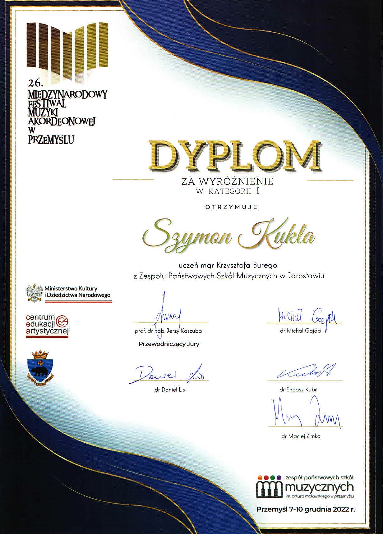 Skan ozdobnego dyplomu na białym tle stylizowane w odcieniach niebieskiego przeciwległe rogi - lewy dolny - prawy górny, po lewej stronie na górze logo 26 Międzynarodowego Konkursu Akordeonowego w Przemyślu, poniżej dużymi literami napis DYPLOM za wyróżnienie w kategorii I otrzymuje Szymon Kukla uczeń mgra Krzysztofa Burego z ZPSM w Jarosławiu, po lewej logotypy MKiDN, CEA oraz miasta Przemyśl, po prawej na dole logotyp ZPSM im. F. Chopina w Jarosławiu