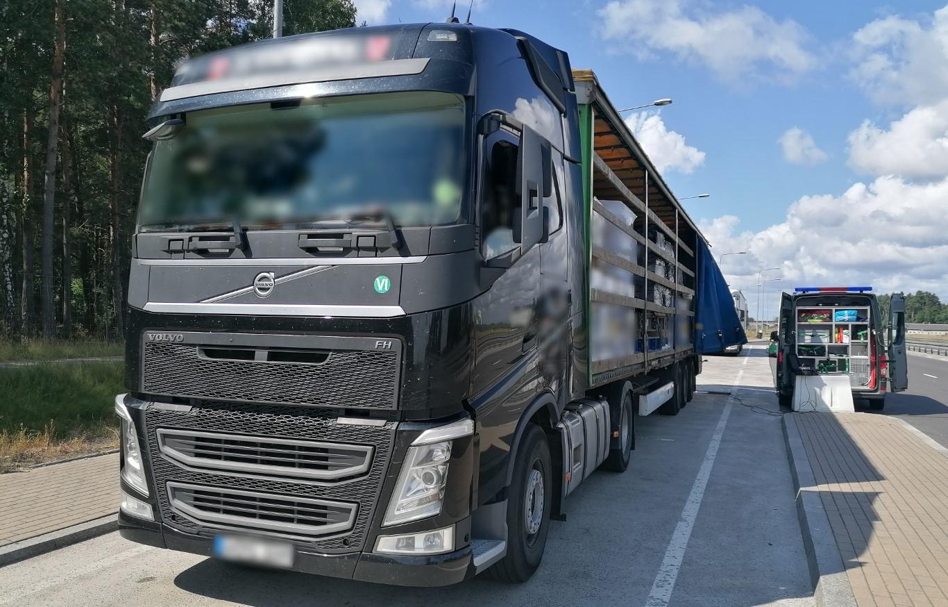 Po lewej stronie stoi ciężarówka z odsuniętą plandeką na naczepie. Po prawej stronie stoi radiowóz ITD.