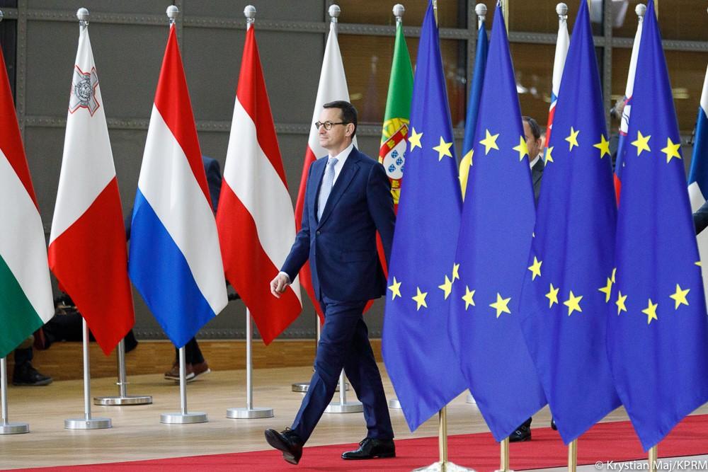 Premier Mateusz Morawiecki wychodzi zza rzędu flag państw.