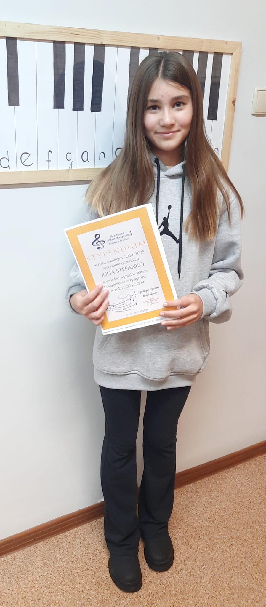 Na zdjęciu widoczna jest uczennica trzymająca w rękach dyplom stypendialny.