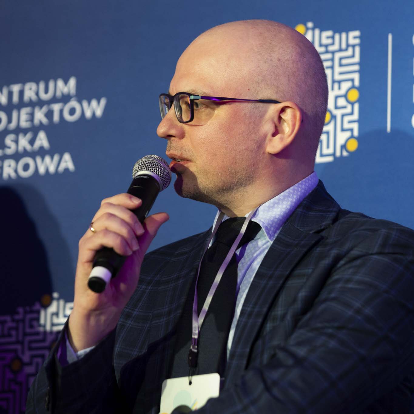 Profesor Piotr Szczuko trzyma mikrofon i mówi do niego.