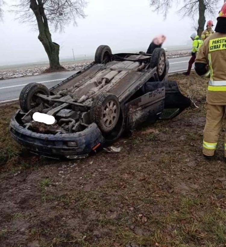 Wypadek samochodu osobowego. Pojazd leży na dachu obok jezdni.