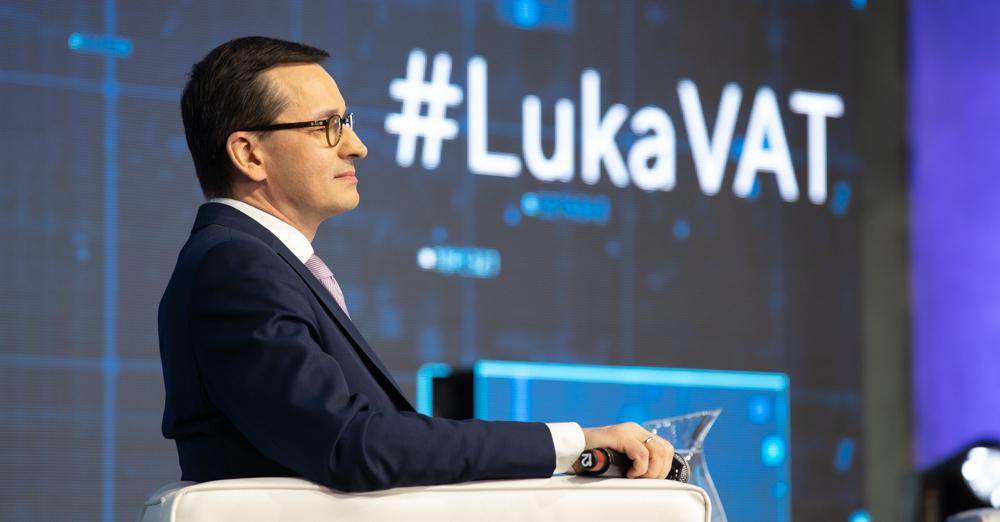 Premier Mateusz Morawiecki siedzi, a za nim na ekranie wyświetla się napis #LukaVAT.