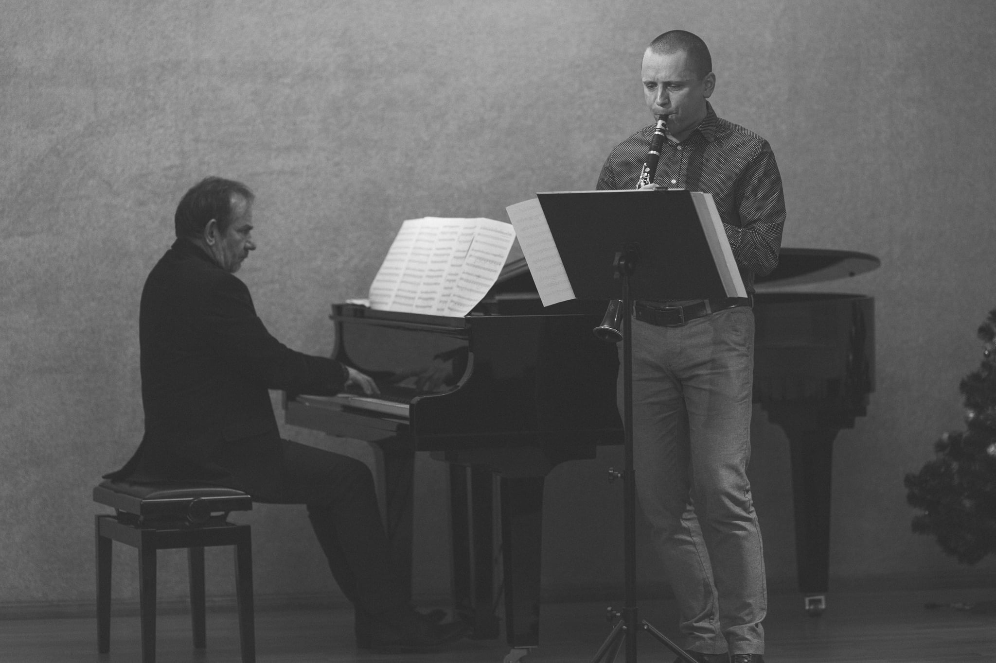 Czarno-biała fotografia przedstawiająca Pana dr Pawła Kroczka grającego na klarnecie i Pana Andrzeja Bednarskiego przy fortepianie. Zdjęcie wykonane w auli szkolnej w dniu 17 grudnia 2021 r.
