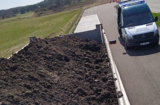 Niezabezpieczona plandeką ziemia na wywrotce i stojący obok niej radiowóz ITD.