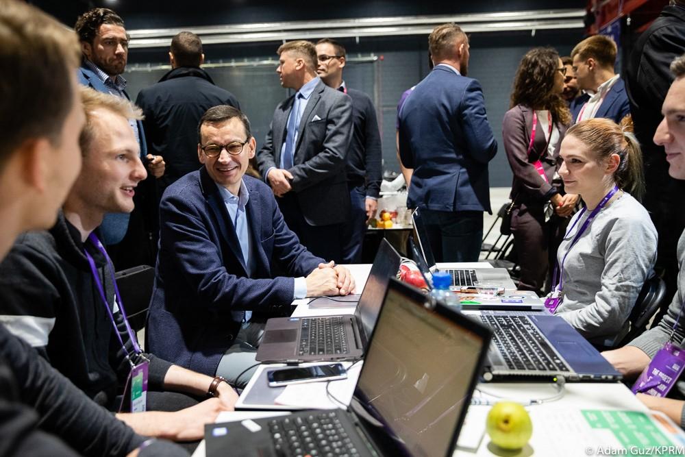 Premier Mateusz Morawiecki siedzi i rozmawia z programistami.