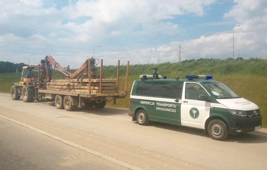 Radiowóz ITD i traktor ciągnący przyczepę z płytami betonowymi