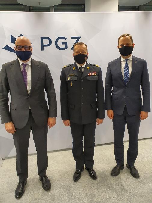 Zastępca komendanta głównego Państwowej Straży Pożarnej w towarzystwie dwóch przedstawicieli przemysłu zbrojeniowego, w tle ściana z logiem Polskiej Grupy Zbrojeniowej