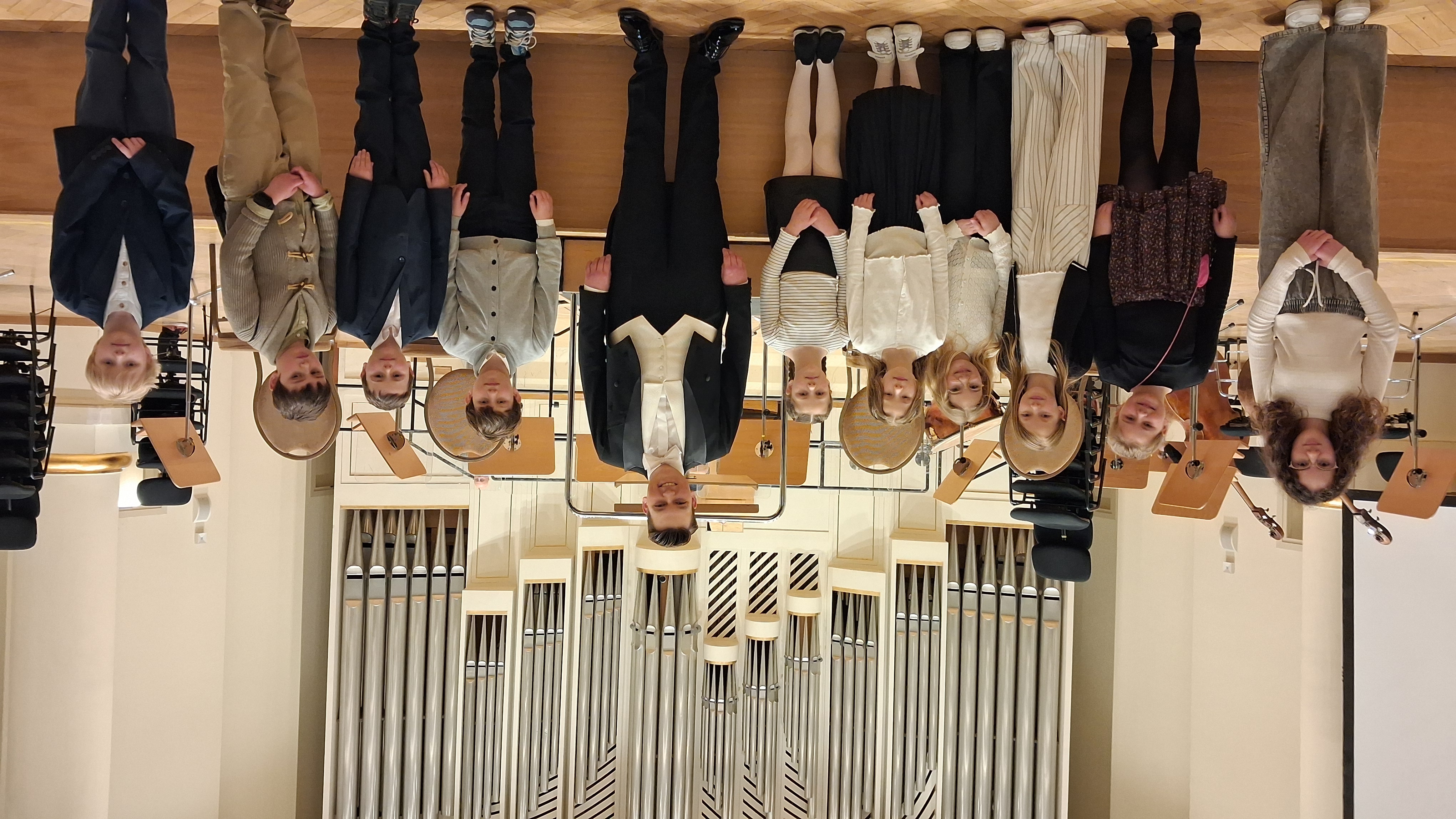 Grupa dzieci i dyrygent na scenie sali koncertowej z organami w tle