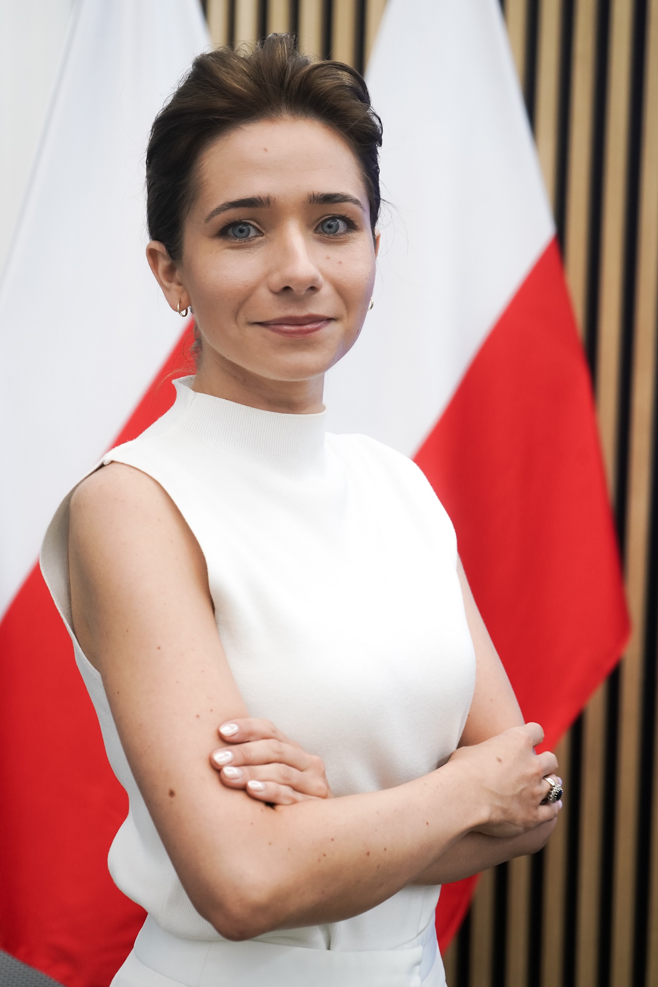 Adrianna Całus-Polak w białym ubraniu stoi na tle polskiej flagi.