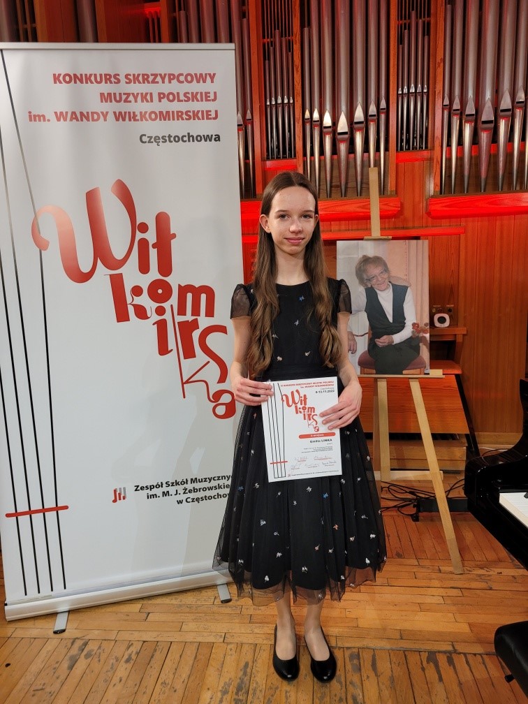 Na zdjęciu Emilia Linka z dyplomem Konkursu Skrzypcowego. W tle biały baner Konkursu Muzyki Skrzypcowej w Częstochowie.