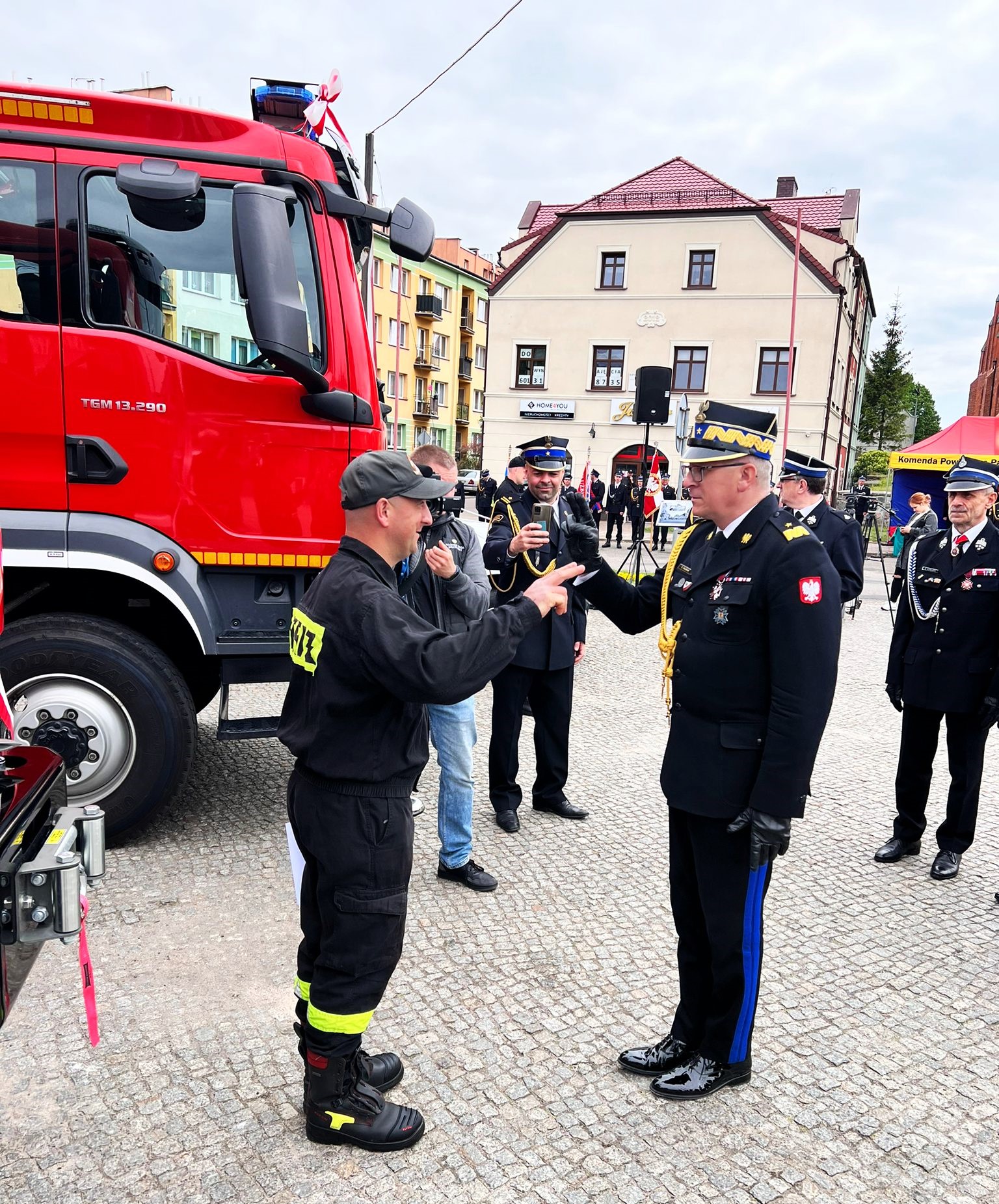 Zastępca komendanta głównego PSP salutuje wspólnie ze strażakiem - kierowcą, który stoi obok przekazanego samochodu ratowniczo - gaśniczego