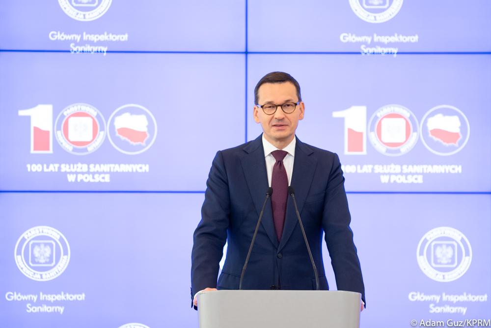 Premier Mateusz Morawiecki podczas przemówienia na tle ścianki wizyjnej.