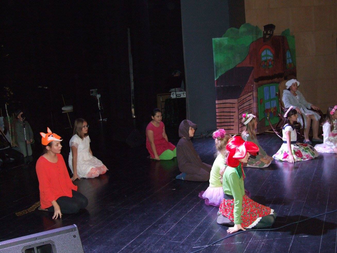 Zdjęcie przedstawia grupę dzieci siedzących na podłodze. Mają one na sobie różne przebrania. np. lisa, wilka oraz kwiatów.