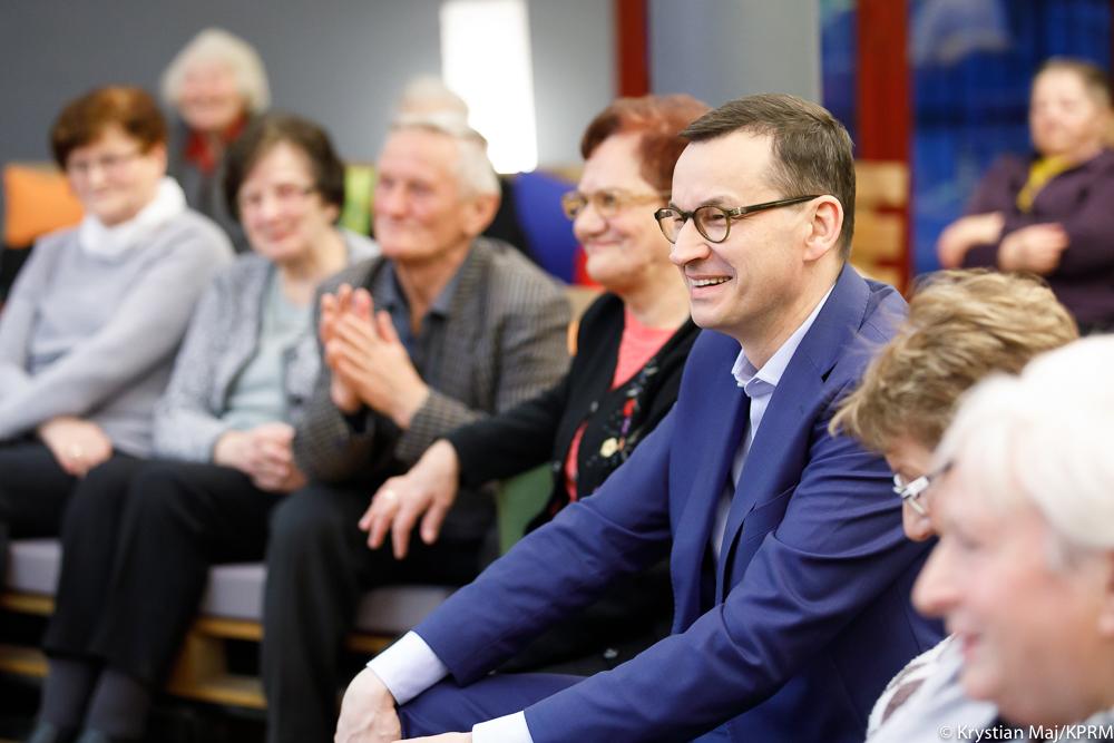 Premier Mateusz Morawiecki siedzi wśród emerytów.