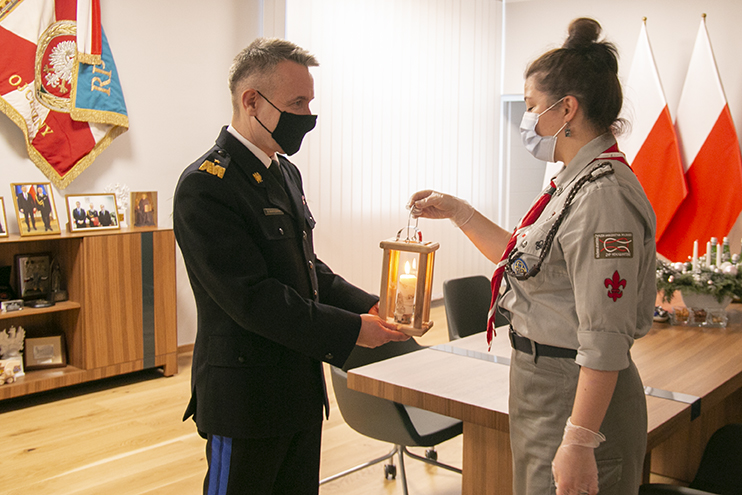 Harcerka z Zarządu Związku Harcerstwa Polskiego przekazujei Betlejemskie Światełko Pokoju na ręce Komendanta Głównego PSP. W tle Sztandar PSP