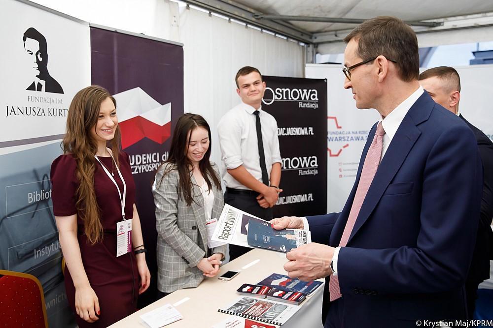 Premier Mateusz Morawiecki przegląda publikacji przy stoisku.