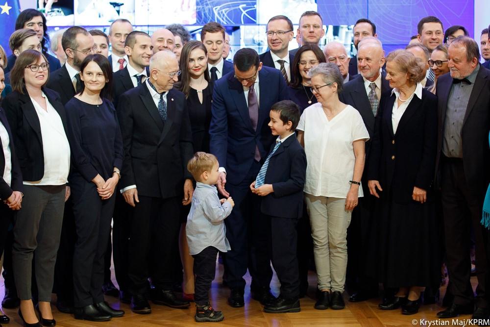 Premier Mateusz Morawiecki wita się z małych chłopcem, a obok pozują do zdjęcia laureaci.