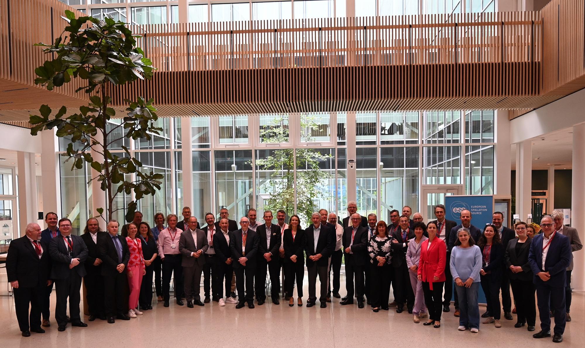 Zdjęcie zbiorowe - w dużym korytarzu stoi grupa kilkudziesięciu osób, za nimi z lewej drzewo w doniczce, w tle przeszklone wejście.