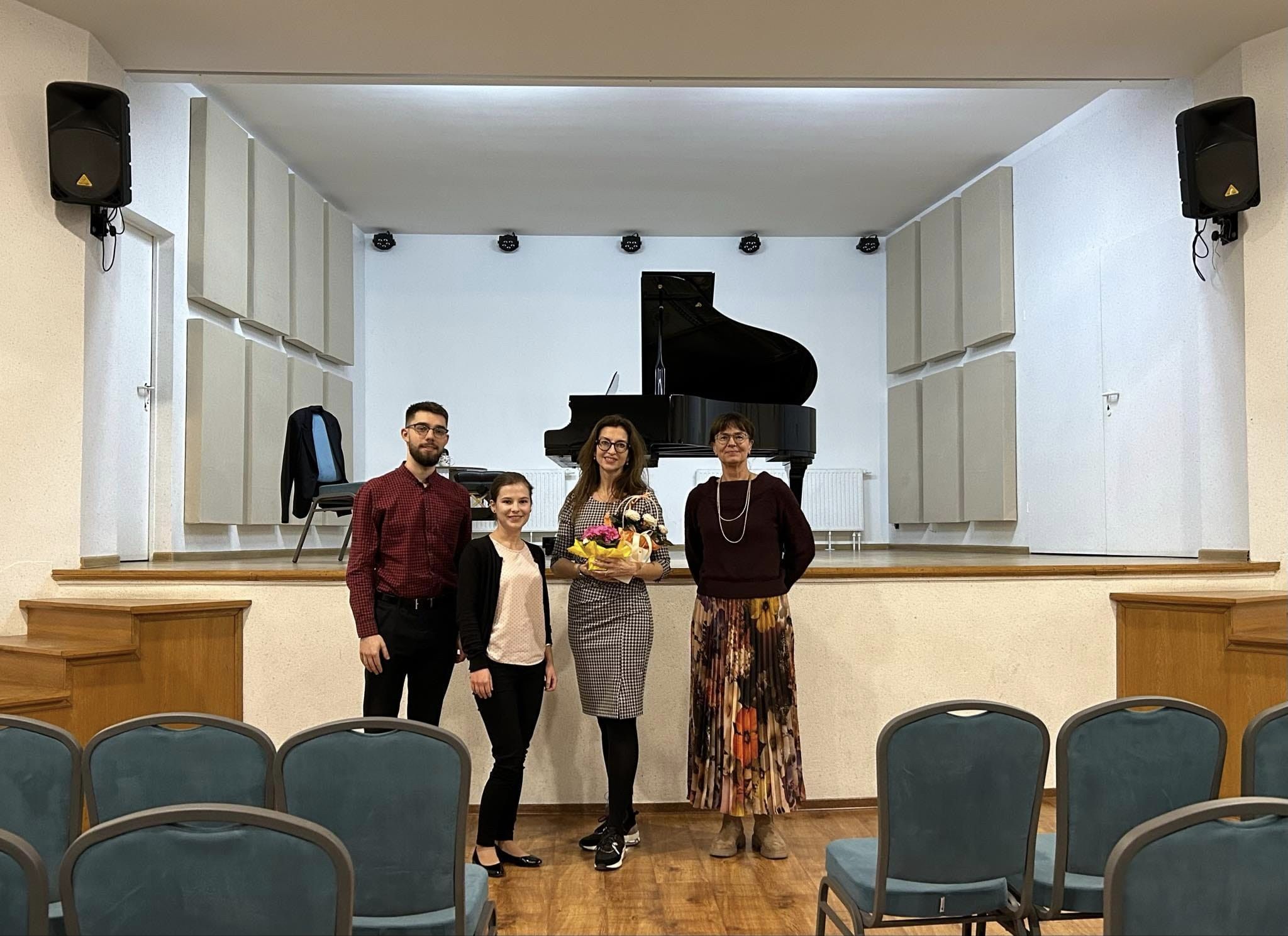 Zdjęcie przedstawia grono pedagogiczne z prowadzącą warsztaty na tle sali koncertowej. 