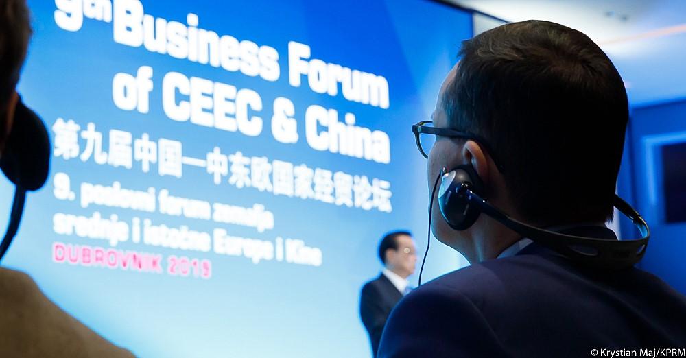 Premier Mateusz Morawiecki patrzy na prezentację ze słuchawkami na uszach.