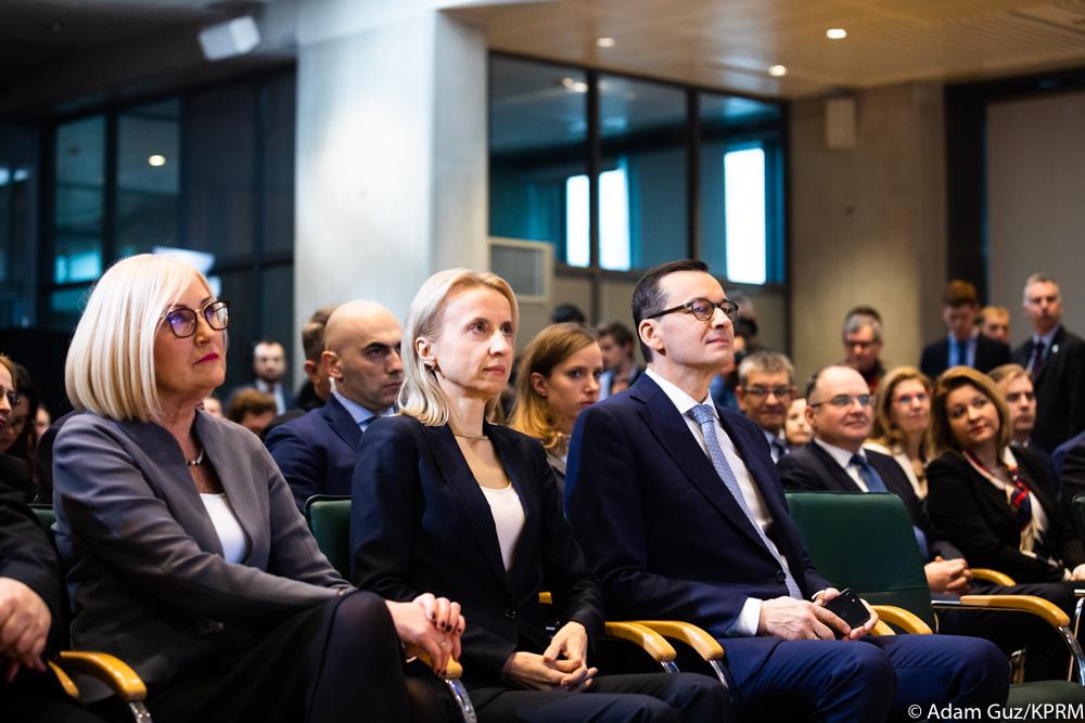 Od lewej, minister Joanna Kopcińska, minister finansów Teresa Czerwińska i premier Mateusz Morawiecki siedzą, a w tle uczestnicy konferencji.