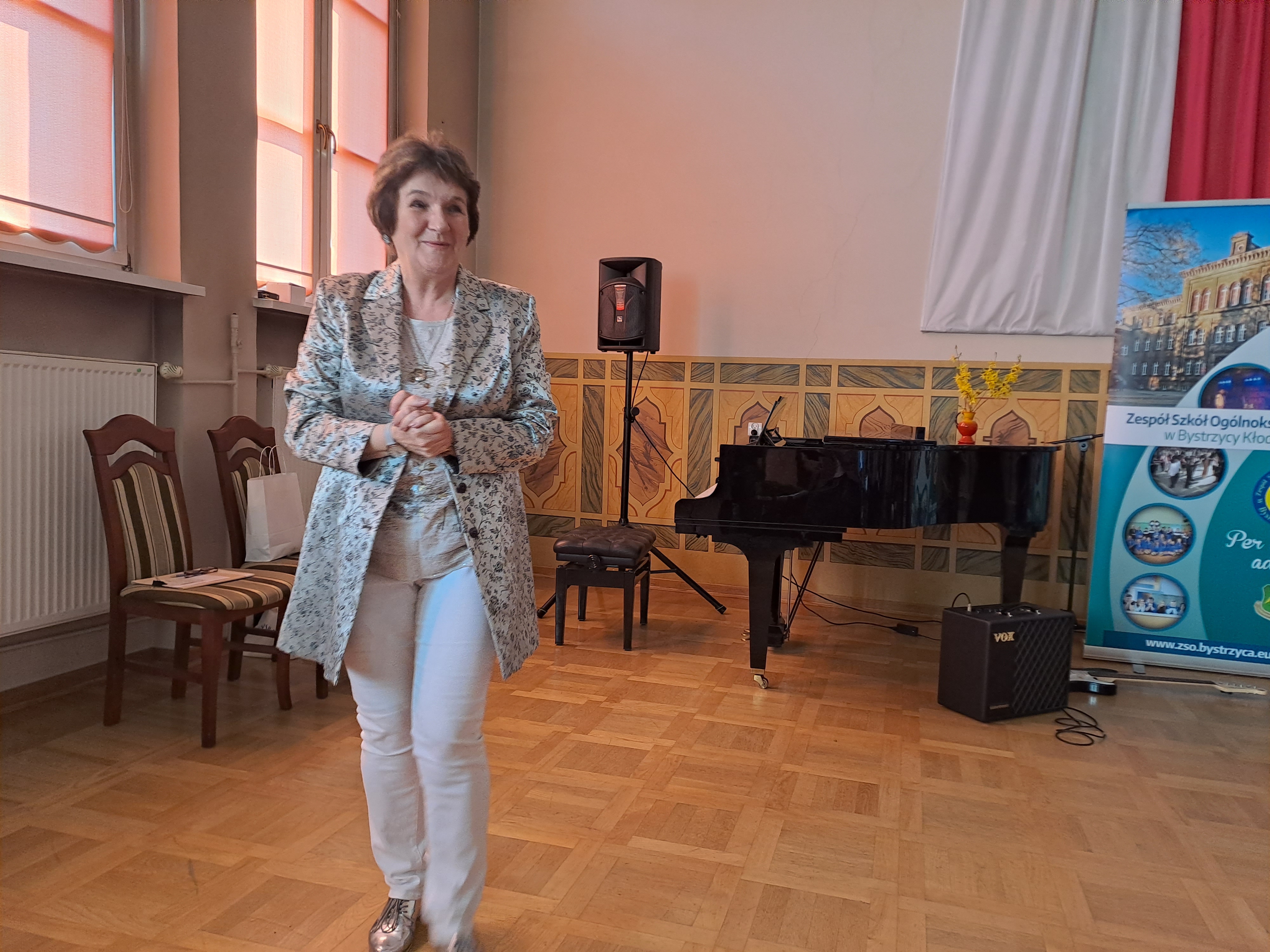 Idąca Pani Elżbieta Kubicz w tle widoczny fortepian.