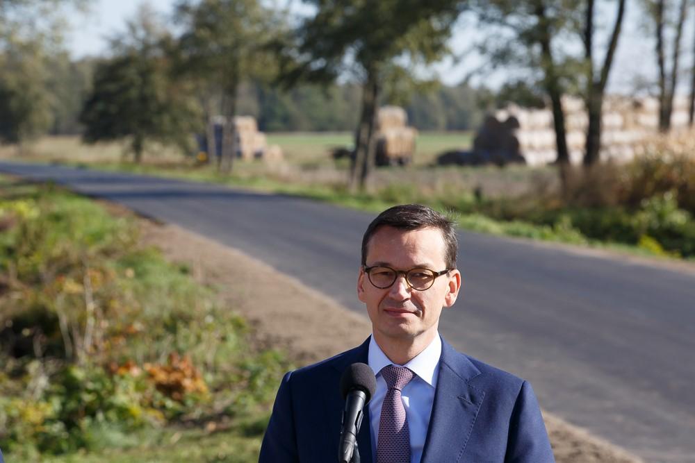 Premier Mateusz Morawiecki stoi przy mikrofonie, w tle droga.