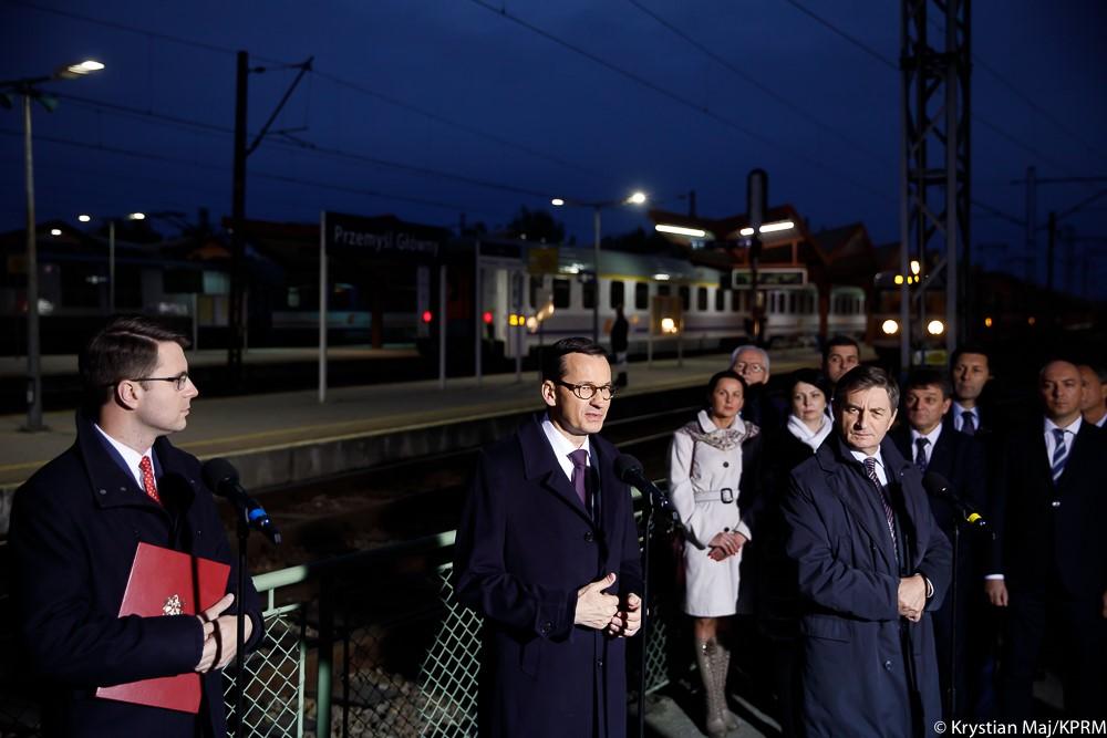 Uczestnicy konferencji stoją na dworcu przy mikrofonach.