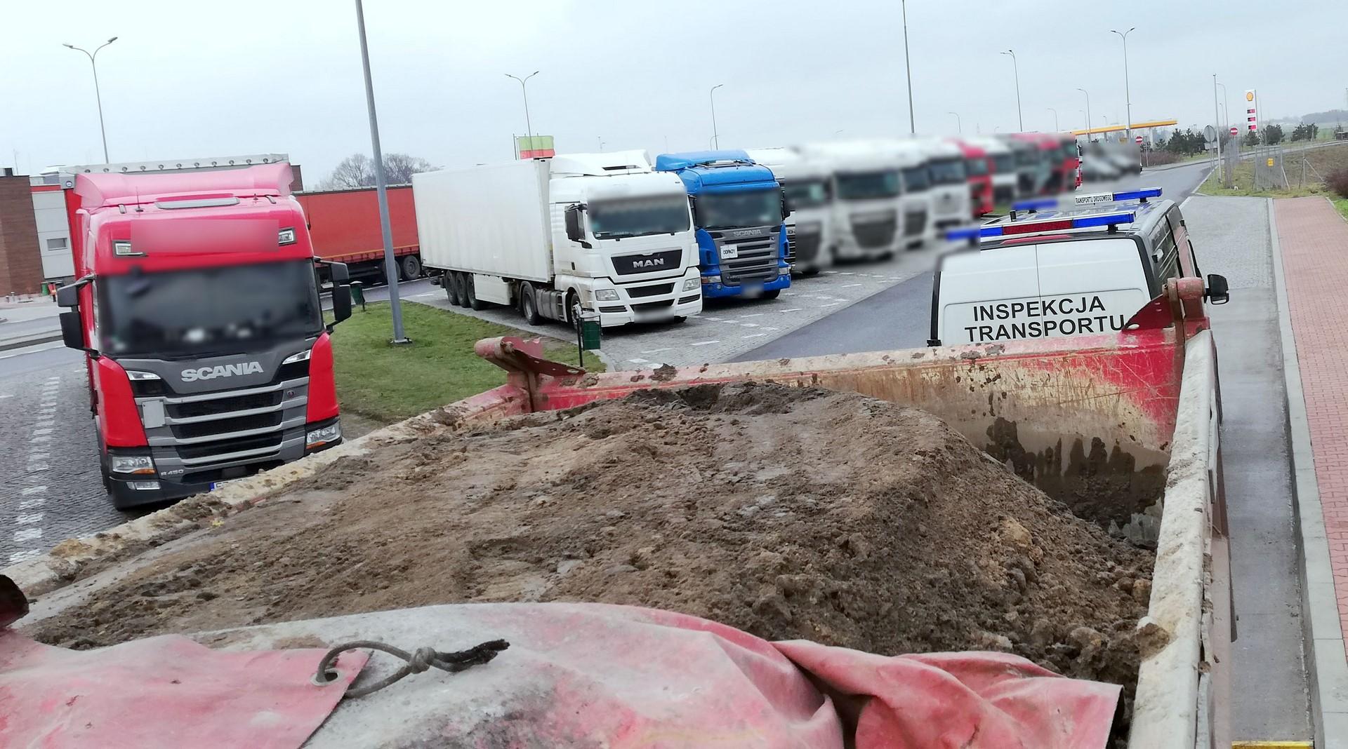 Nieprzykryta plandeką ziemia za zatrzymanej wywrotce i radiowóz ITD.