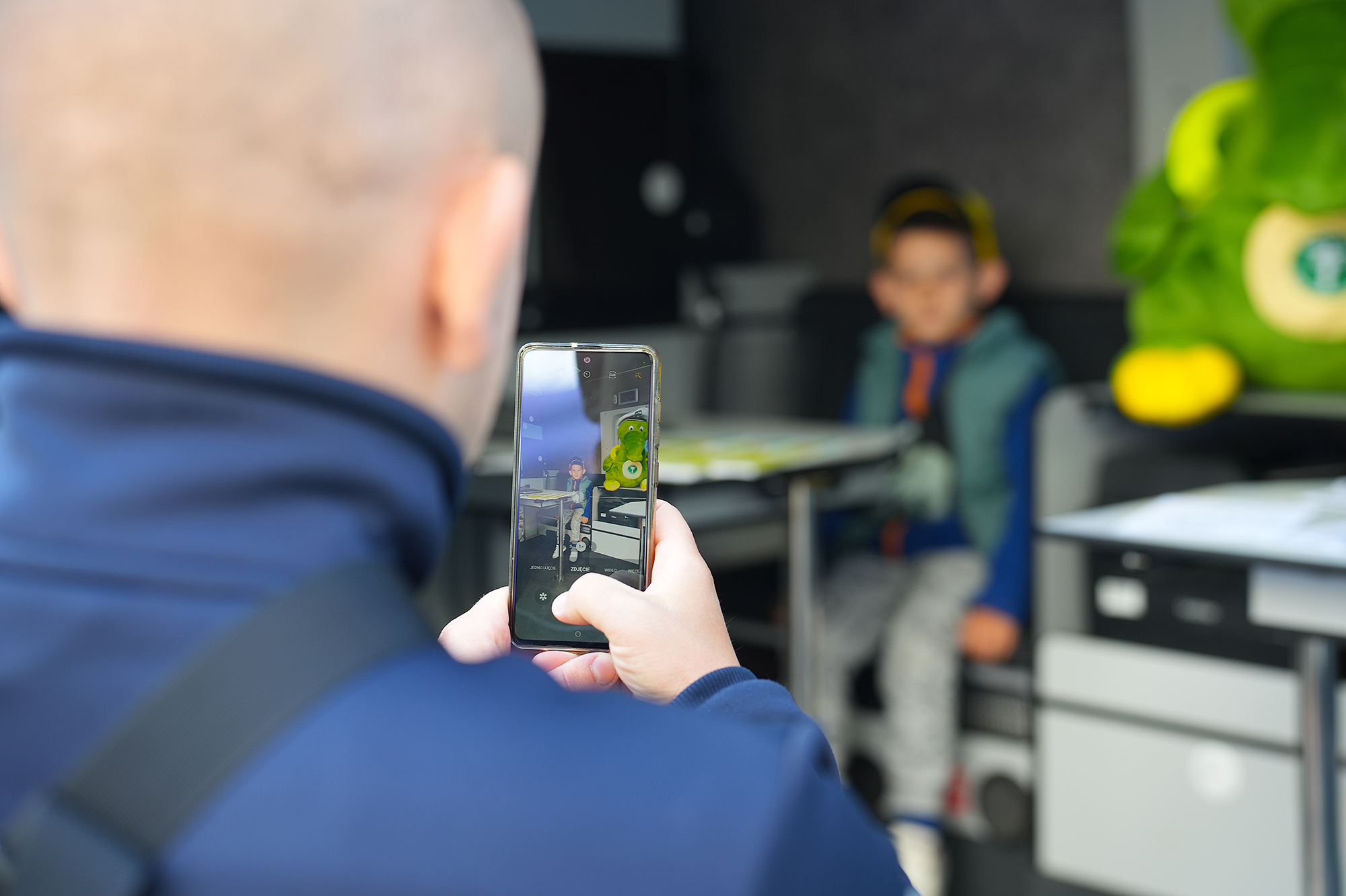 Chłopiec w inspekcyjnym furgonie - mężczyzna trzyma w ręku telefon, którym robi chłopcu zdjęcie. Obok chłopca jest Krokodylek Tirek.
