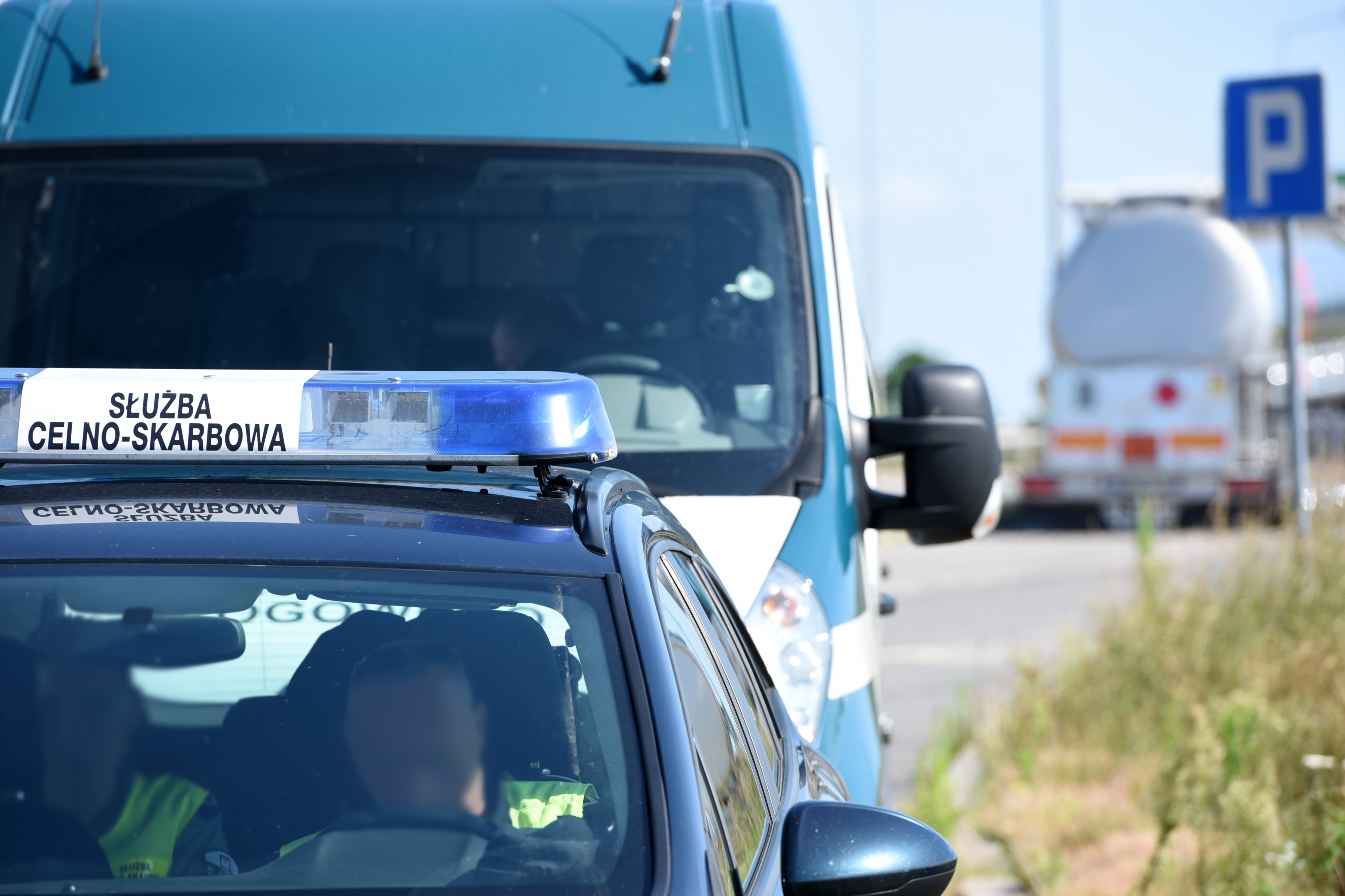 Radiowóz osobowy z belką na dachu z napisem Służba Celno-Skarbowa, a za nim radiowóz typu bus ITD. W tle kontrolowane ciężarówki.