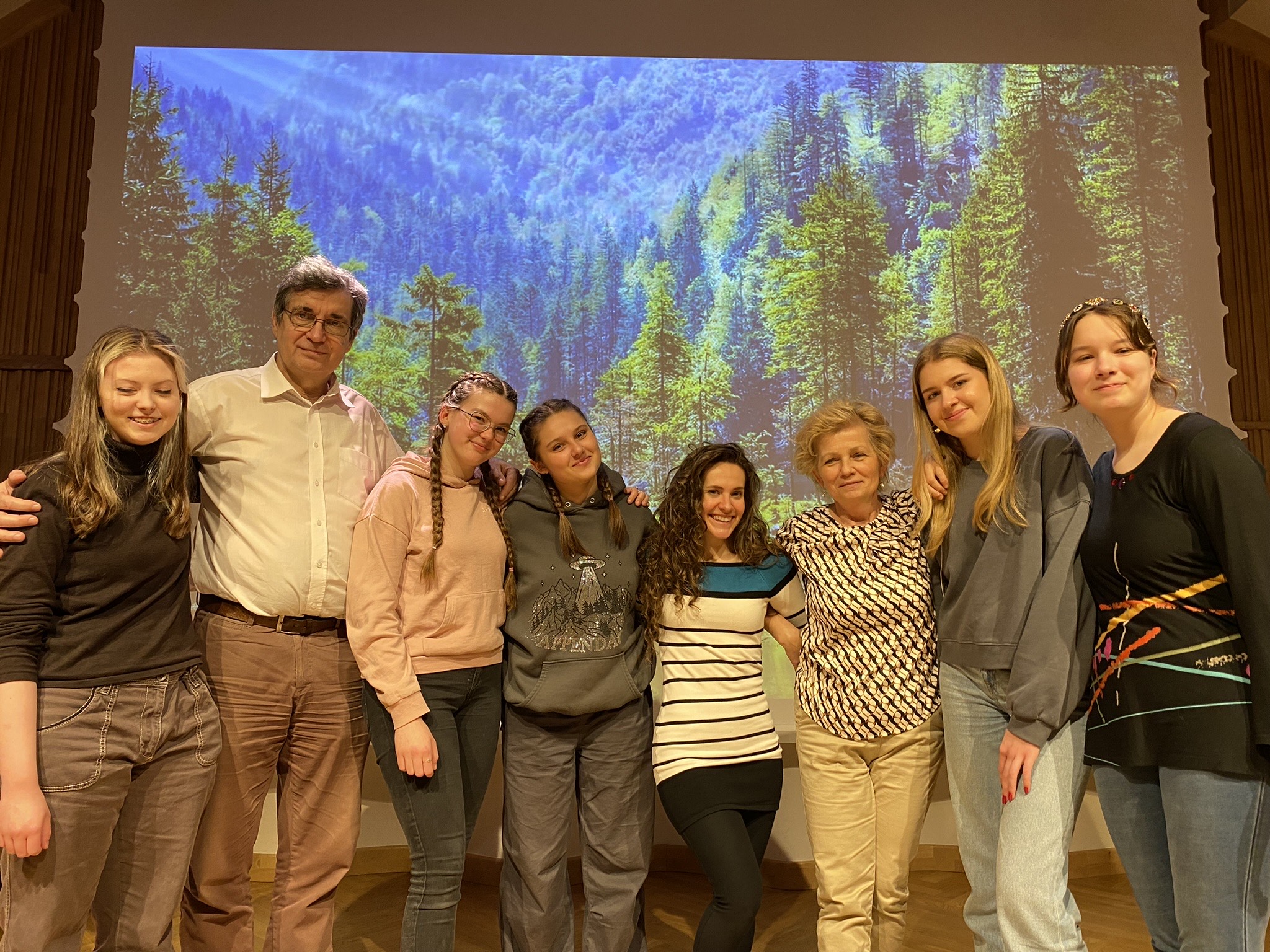 Zdjęcie. Na estradzie stoi grupa uczestników warsztatów musicalowych. W tle na dużym ekranie wyświetlony jest obraz lasu w górach.