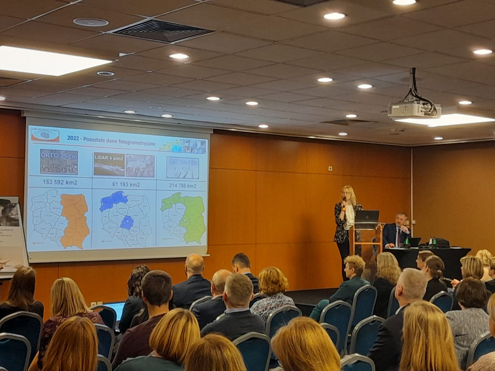 Zdjęcie przedstawia Dyrektor Departamentu Geodezji, Kartografii i Systemów Informacji Geograficznej - Annę Bober w trakcie prezentacji oraz Głównego Geodetę Kraju dr. hab. inż. Waldemara Izdebskiego. 