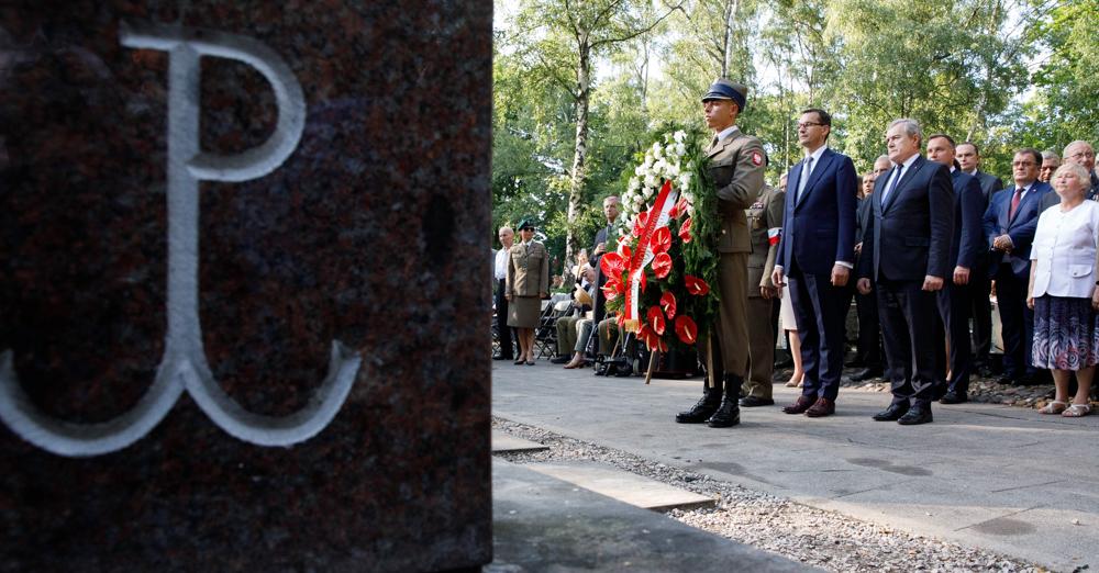 Po lewo znak Polski Walczącej i premier składający kwiaty.