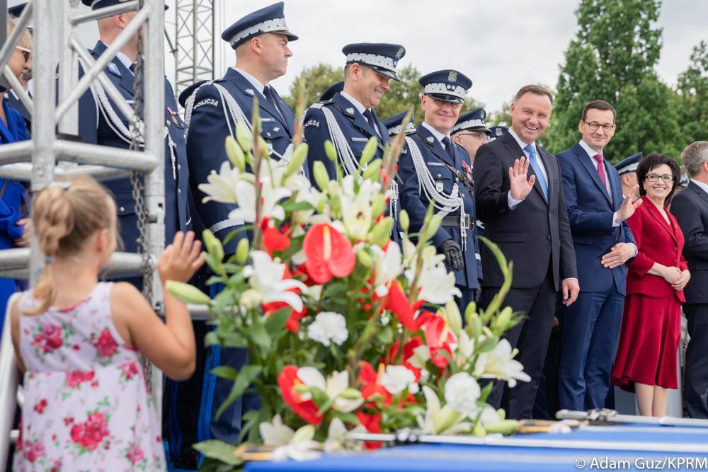 Prezydent Andrzej Duda oraz premier Mateusz Morawiecki machają do dziewczynki podczas uroczystości.