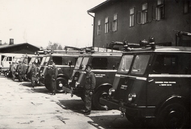 Samochody Zawodowej Straży Pożarnej w 1955 roku stojące przed koszarami obok samochodów stoi kilku strażaków.