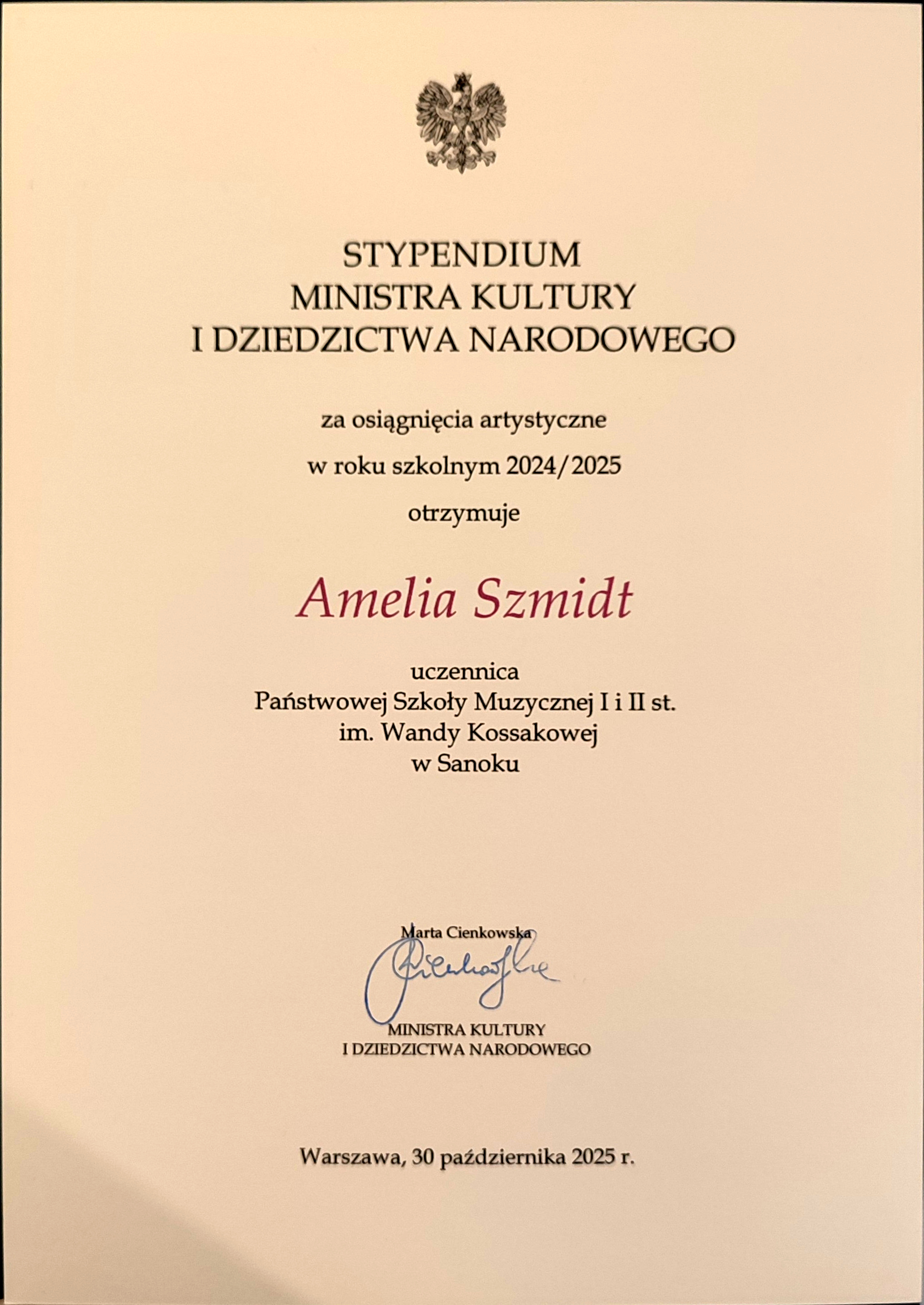 Dyplom stypendium dla Amelii Szmidt za osiągnięcia artystyczne 2025r. Beżowe tło, czarny tekst