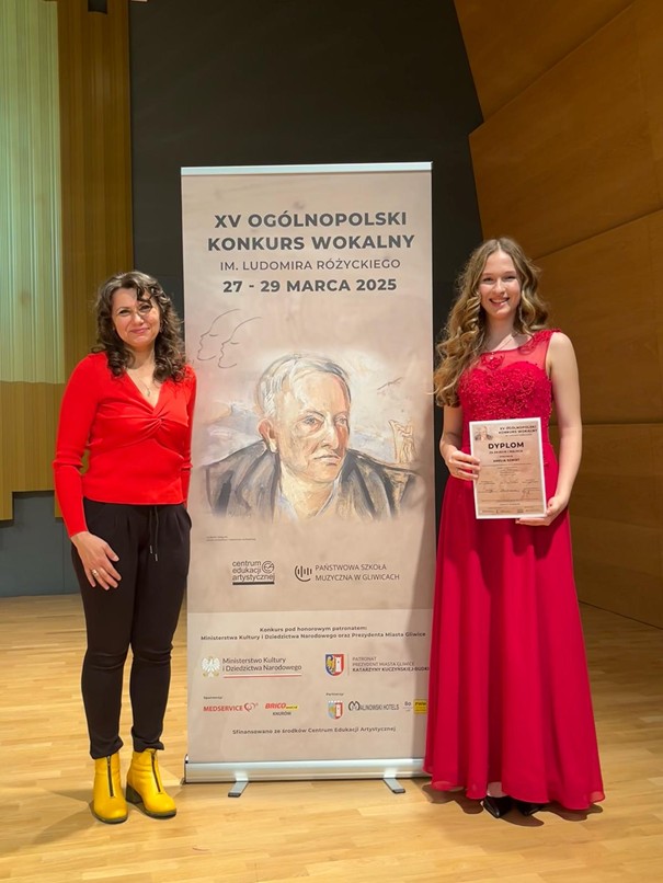 Pani Monika Brewczak i uczennica Amelia Szmidt przy plakacie Ogólnopolskiego Konkursu Wokalnego w Gliwicach.