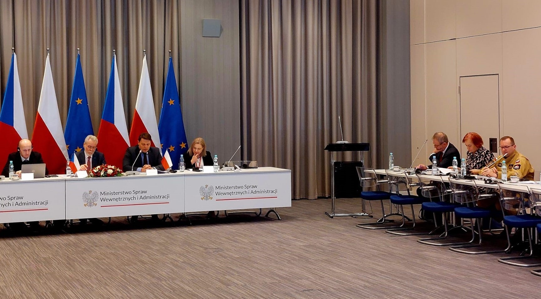 W sali siedzą uczestnicy posiedzenia, za stołem frontowym stoją flagi Czech, Polski i UE. Po prawej stronie sali przy stole siedzi zastępca komendanta głównego PSP
