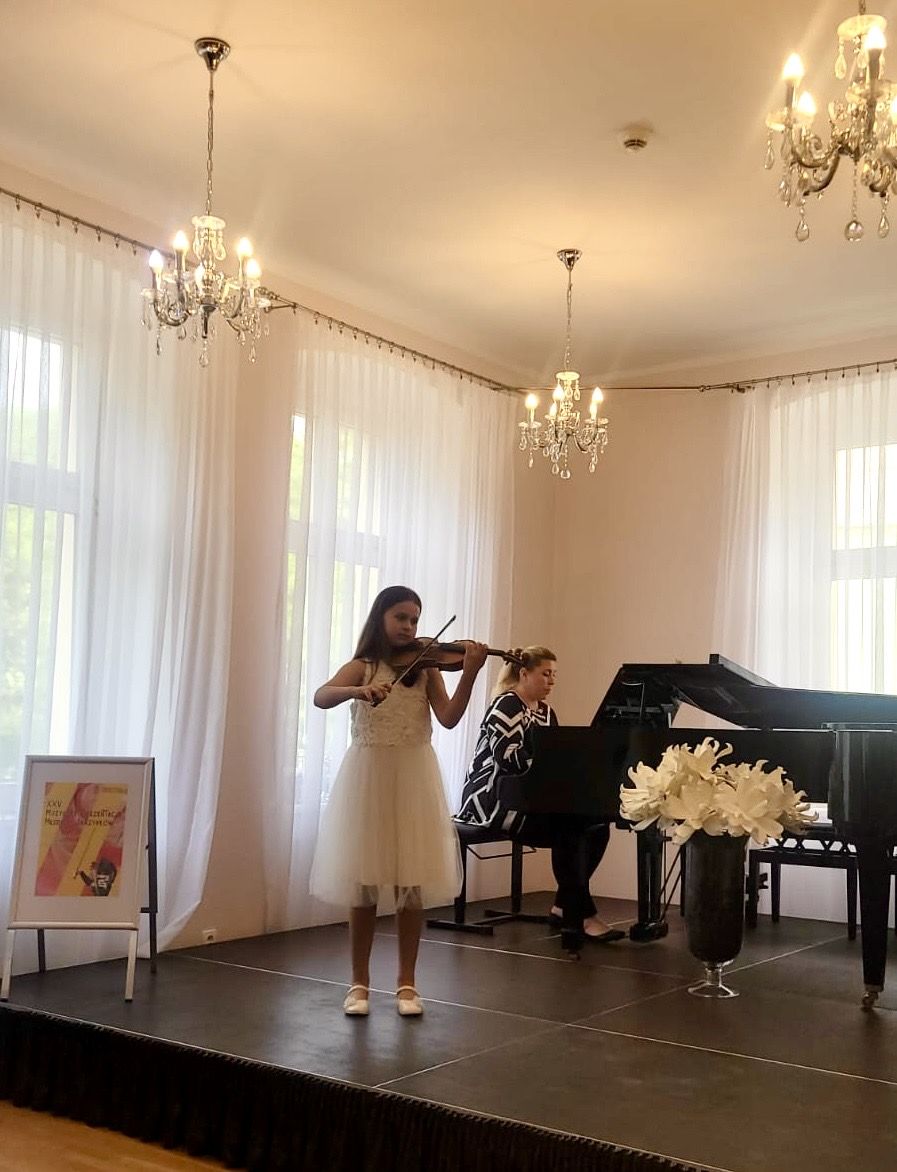 Na zdjęciu widoczna jest grająca na skrzypcach uczennica wraz z akompaniatorem przy fortepianie.