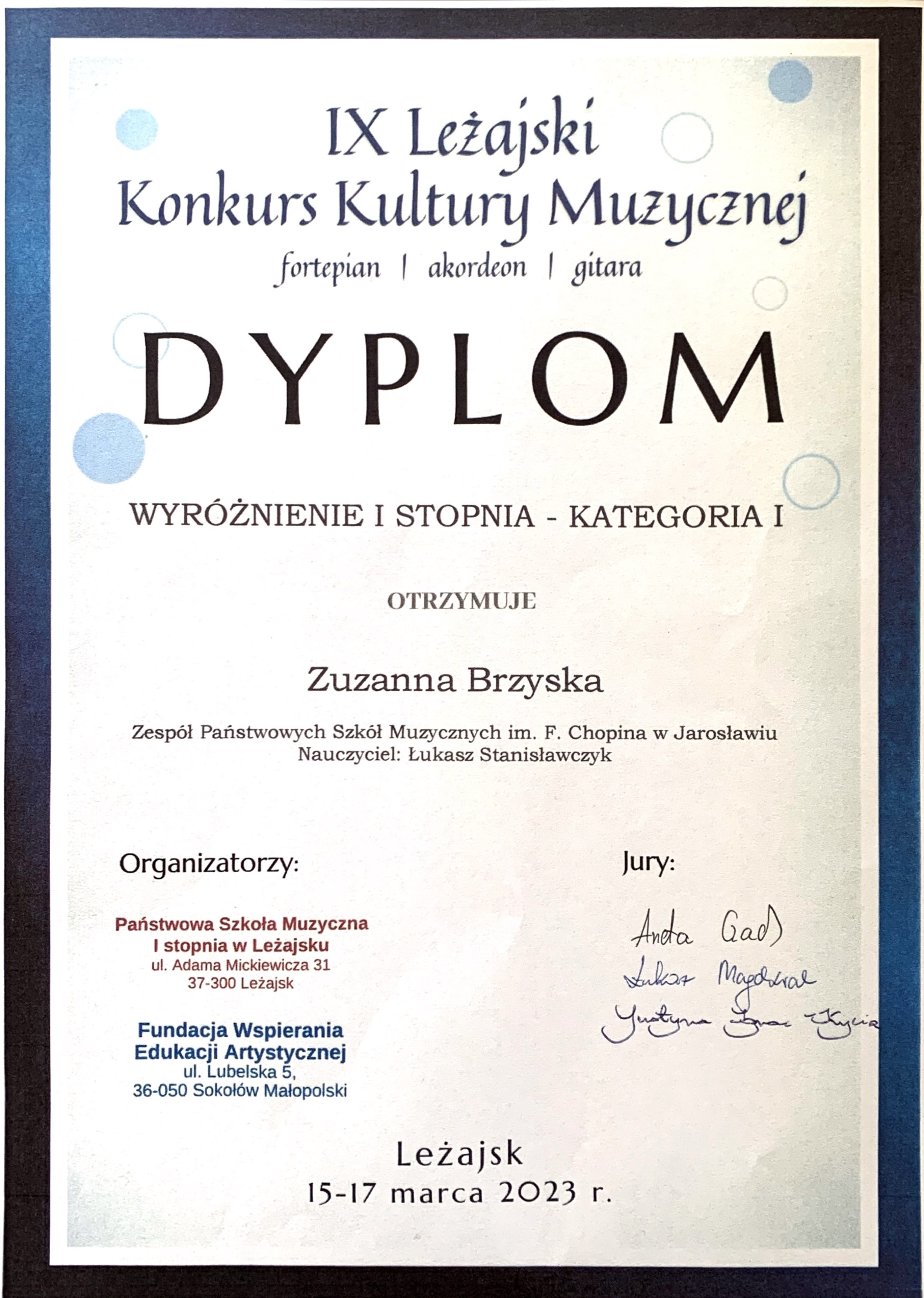 Dyplom konkursu na białym tle z granatowym obramowaniem, na górze granatowymi literami IX Leżajski Konkurs Kultury Muzycznej fortepian/akordeon/gitara Wyróżnienie I stopnia - kategoria I otrzymuje Zuzanna Brzyska ZPSM im. F. Chopina w Jarosławiu Nauczyciel Łukasz Stanisławczyk poniżej z lewej strony pieczątki organizatorów PSM I st. w Leżajsku oraz Fundacji Wspierania Edukacji Artystycznej, po prawej podpisy członków Jury. Na dole napis Leżajsk, 15-17 marca 2023 r.