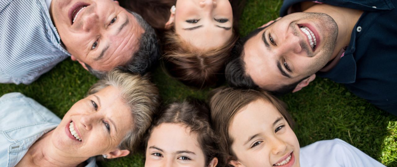 Grupa osób leżących na trawie w okręgu, z głowami skierowanymi do środka.