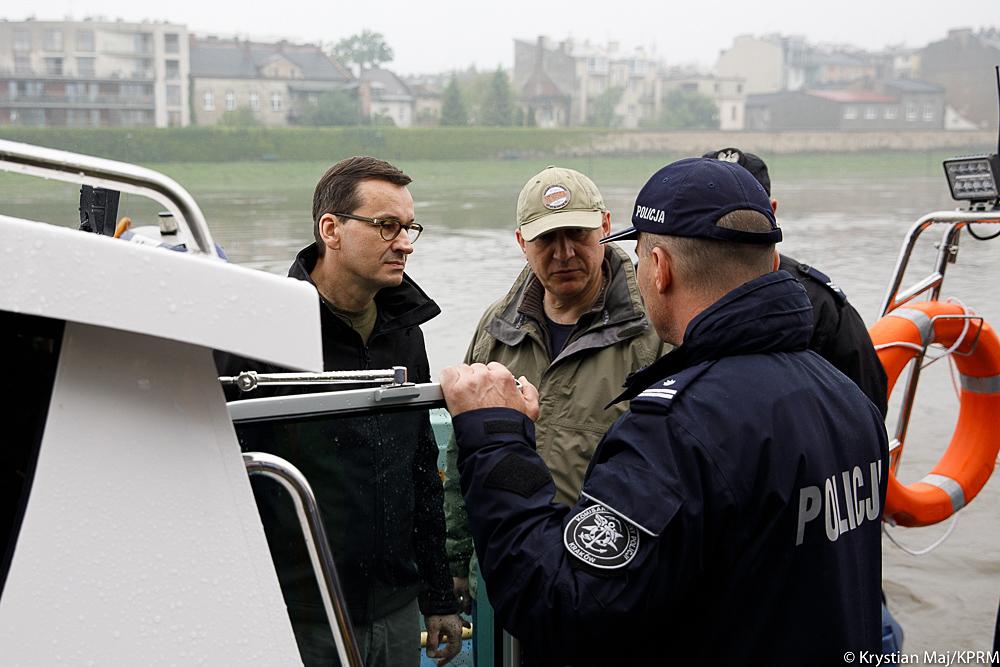 Premier Mateusz Morawiecki i minister Joachim Brudziński rozmawiają z policjantem.