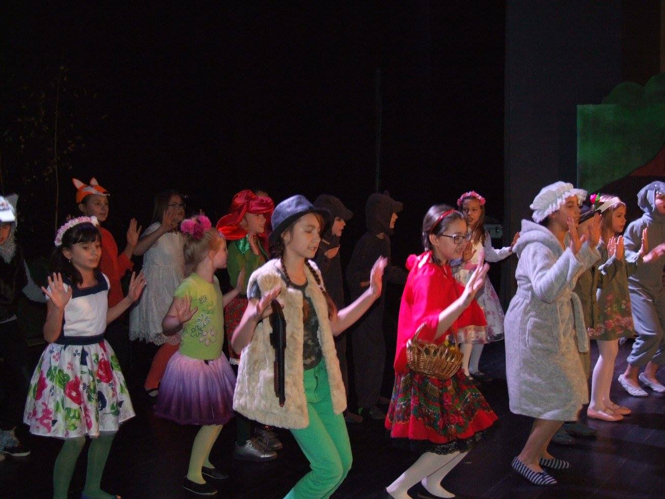 Zdjęcie przedstawia tańczącą grupę dzieci. Są one przebrane m.in za lisa, wilka, Czerwonego Kapturka i babcię.