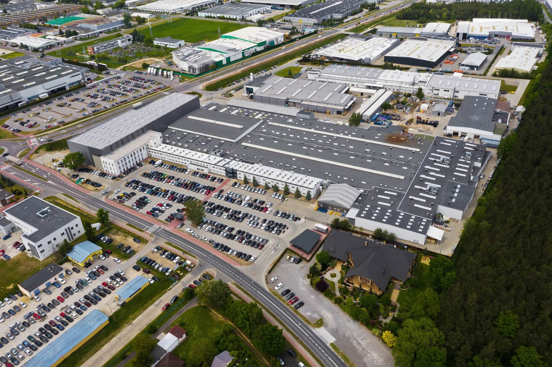 Zdjęcie wykonane z lotu ptaka. Przedstawia rozległe parkingi z autami i hale przemysłowe