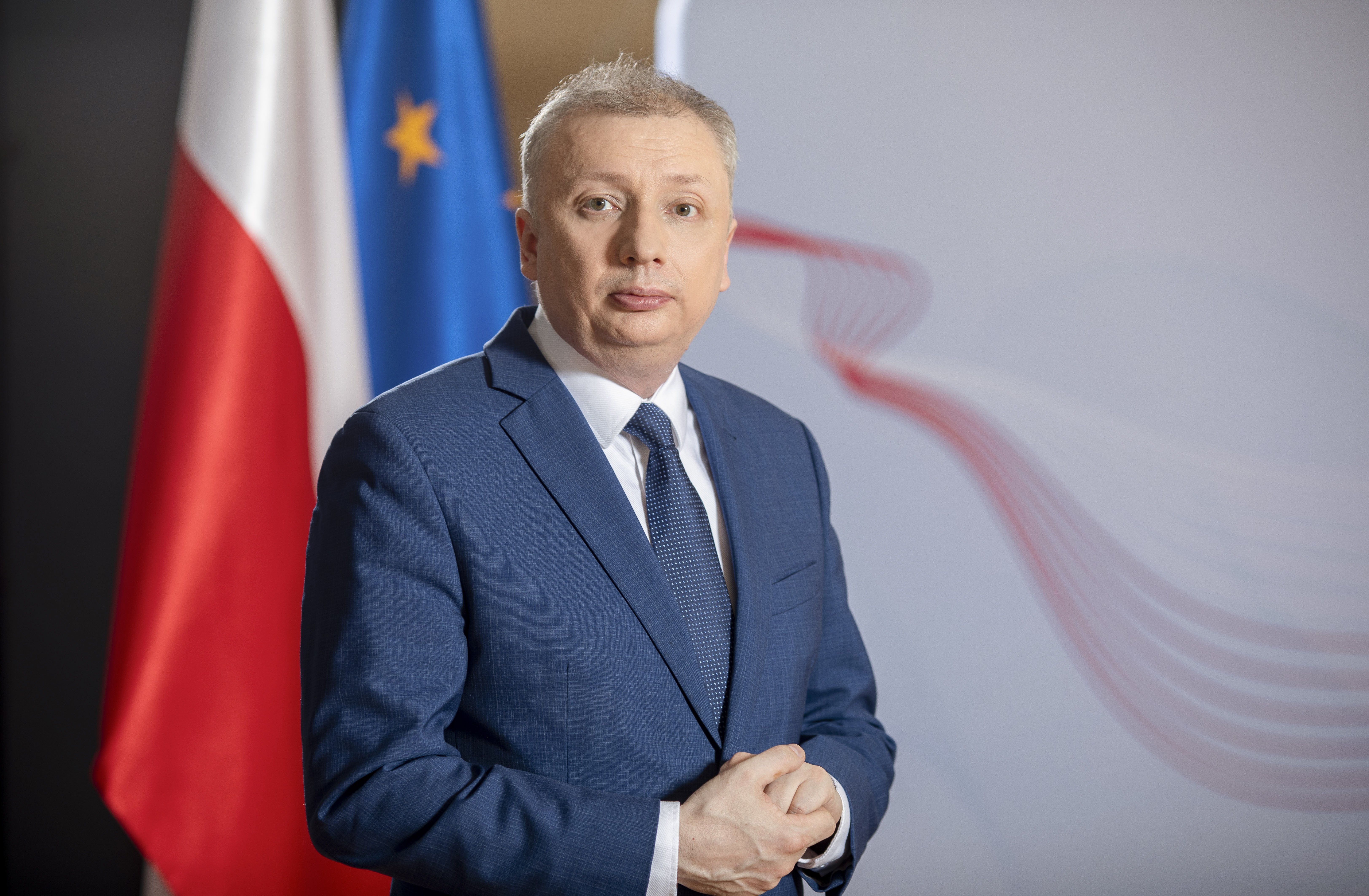 Sebastian Skuza Sekretarz Stanu, Generalny Inspektor Informacji Finansowej na tle flagi Polski i UE