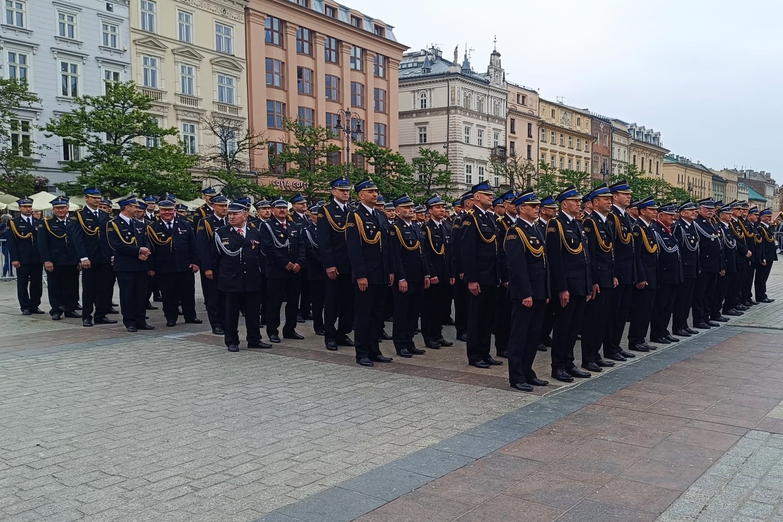Na placu Rynku Głównego w Krakowie stoją w szeregach strażacy w mundurach galowych